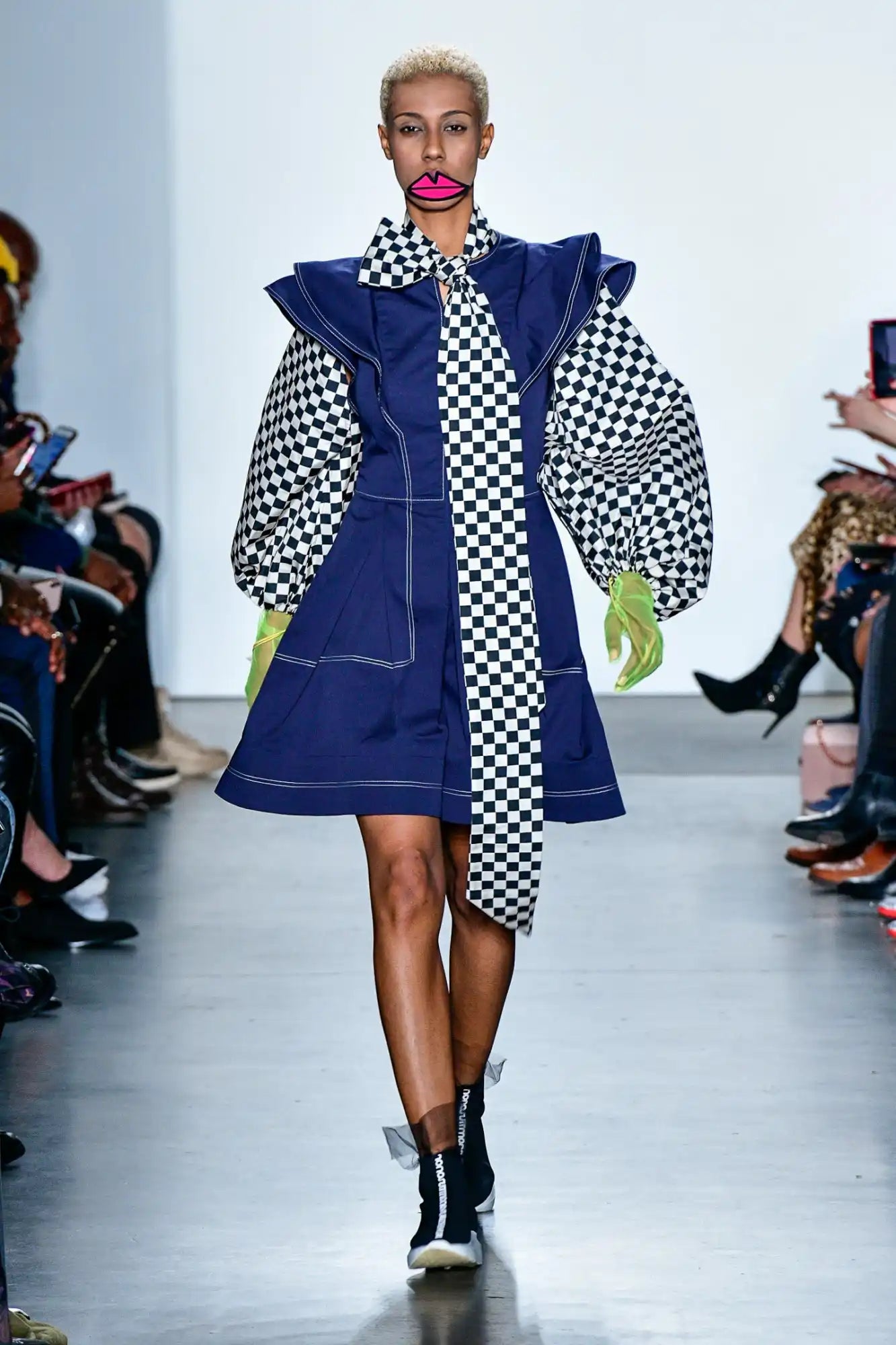 Bold navy blue coat dress with checkerboard pattern accents and dramatic ruffled collar.