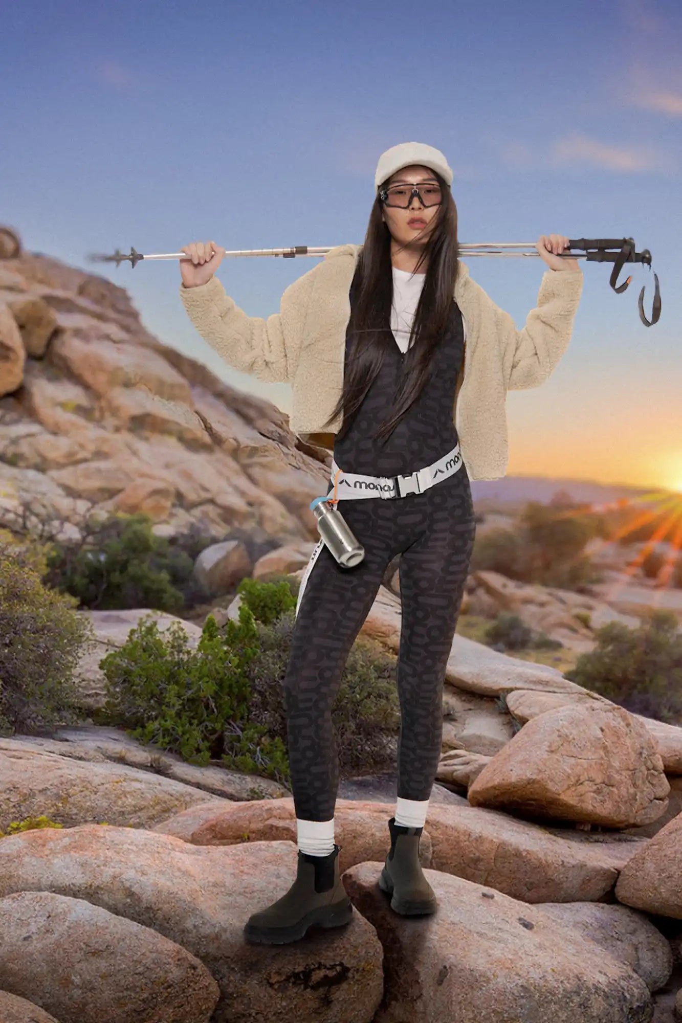 A person in hiking attire posing with a camera strap across their shoulders on rocky terrain.