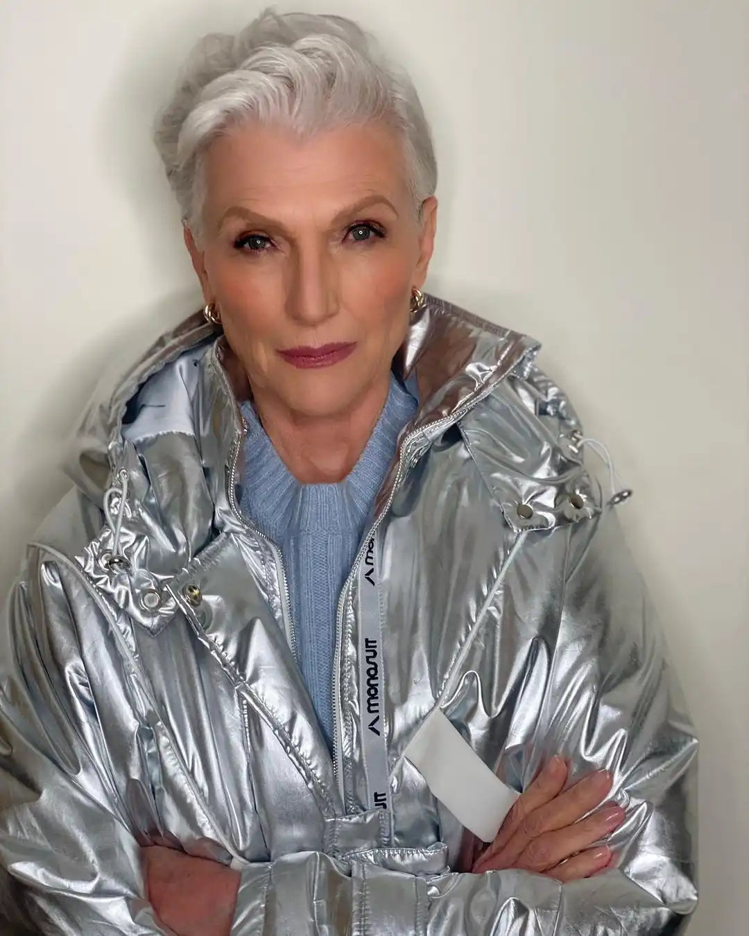 Shiny silver metallic puffer jacket worn with a light blue sweater underneath.